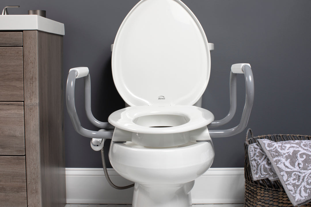 E/R85320H20 ARM Bemis Independence Assurance® with Clean·Shield™, Support Arms, and Personal Wash Bidet is a Plastic 3" Raised Toilet Seat Featuring Stay·Tite® Commercial Fastening System™ and Super·Grip® Bumpers